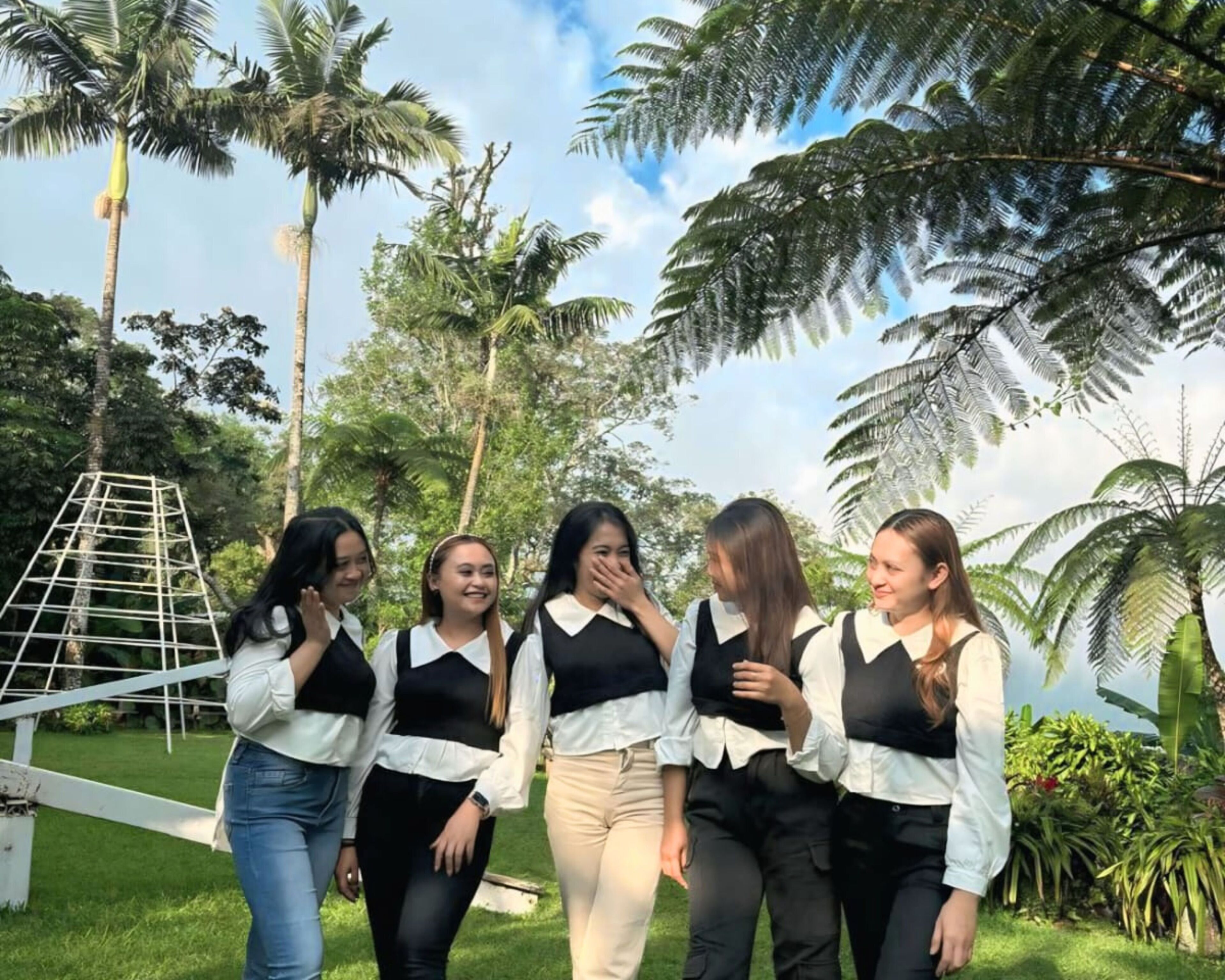 A group of people in a tropical outdoor setting with palm trees and a white structure.