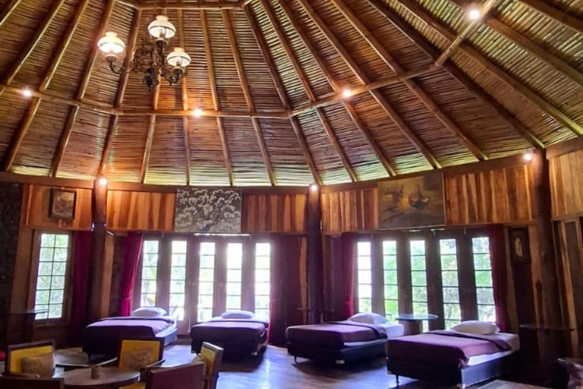 A room with a high wooden ceiling, multiple beds, a dining table, and chairs.