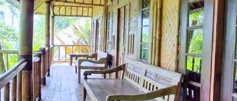 A covered porch with wooden benches and a railing, overlooking a lush garden.