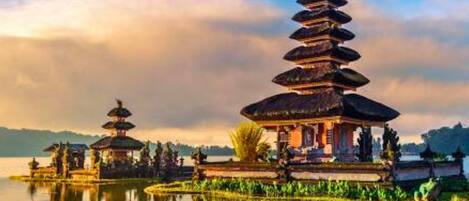 A traditional multi-tiered pagoda structure with a reflection in the water, surrounded by greenery and a clear sky.
