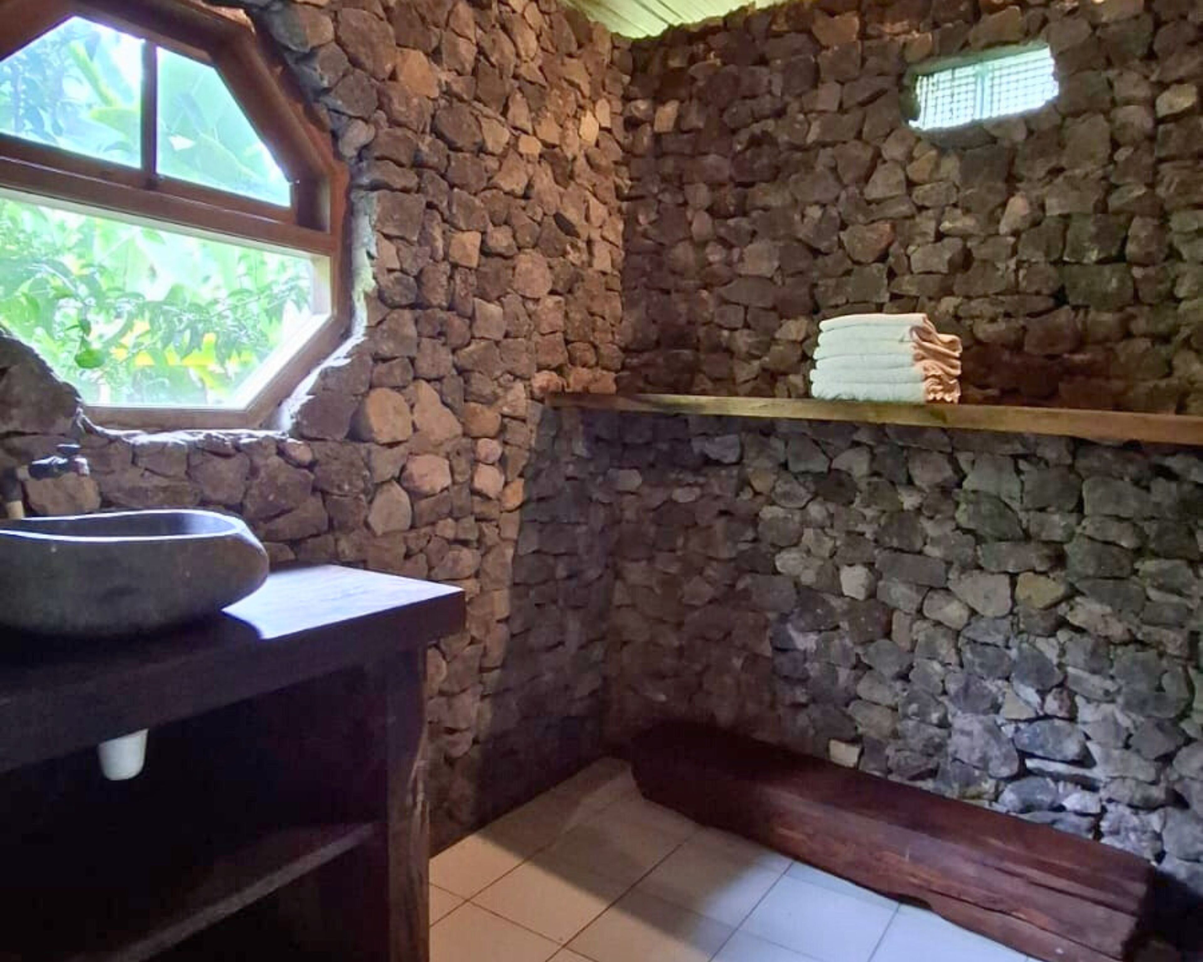 Un baño con paredes de piedra, una ventana, un lavamanos y un perchero para toallas.