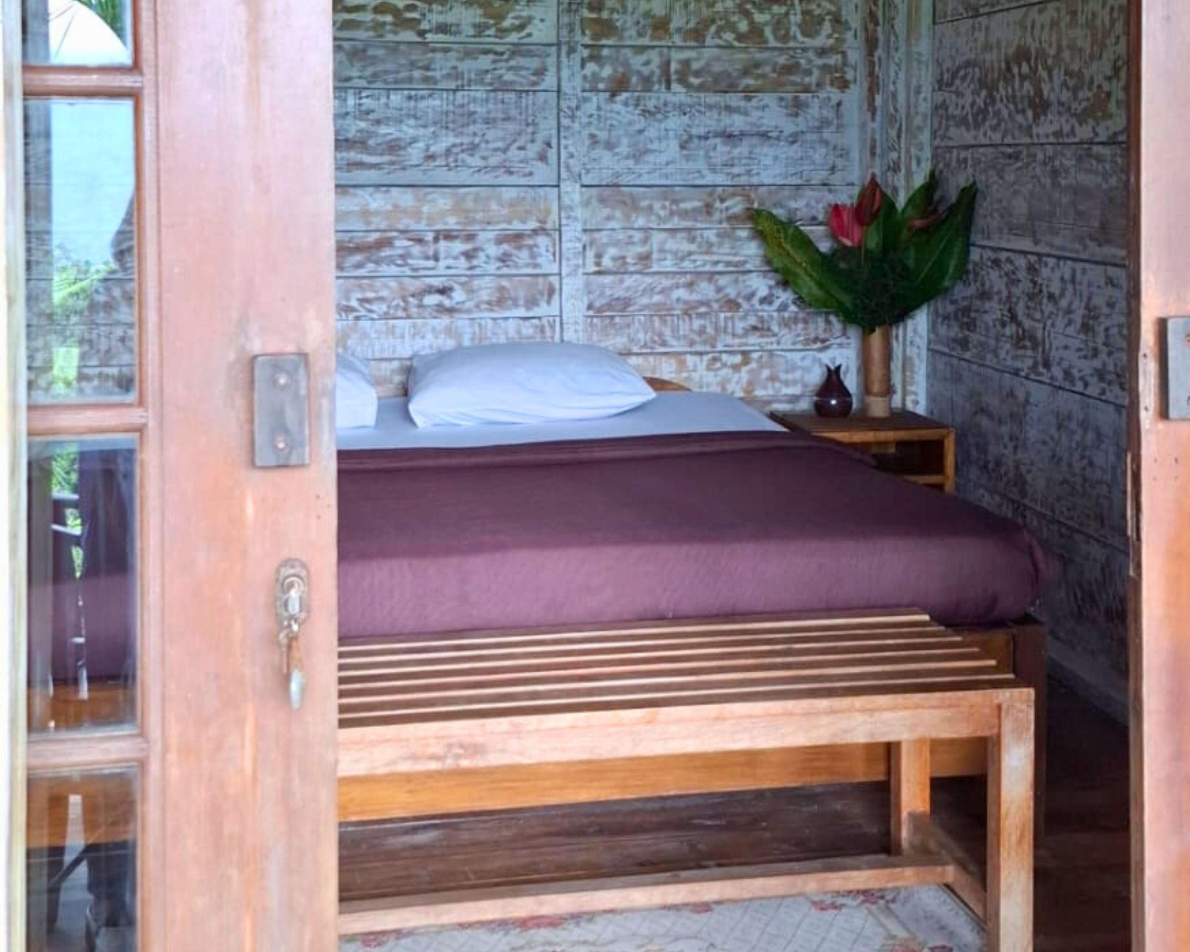 Quarto com cama de madeira, mesa de cabeceira, um vaso com flores e parede rústica.