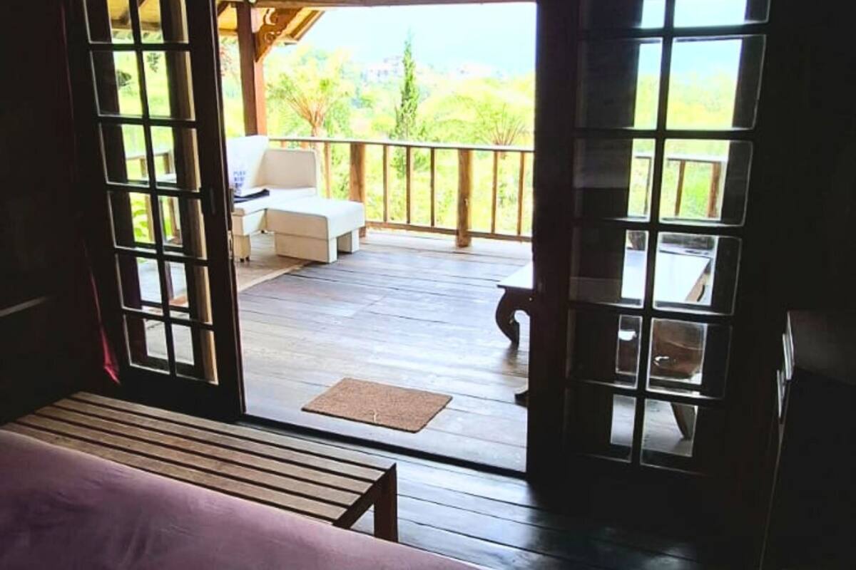A room with a bed, a wooden bench, and a view of an outdoor patio with a sofa and a table.