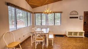 A dining area with a wooden table and chairs, large windows with blinds, a chandelier, and a bench. - Black Bear Retreat - Wonderful 3 bed cabin in Pinetop with a fenced yard & Wifi. (Pinetop)