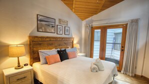 A bedroom with a wooden headboard, a bed with multiple pillows, a nightstand with a lamp, and a view of the outside through a door. - Black Bear Retreat - Wonderful 3 bed cabin in Pinetop with a fenced yard & Wifi. (Pinetop)