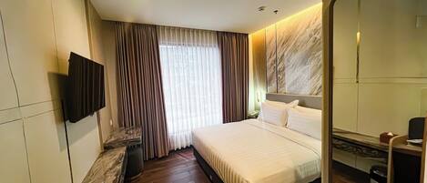 A modern hotel room with a large bed, a flat-screen TV mounted on the wall, a built-in mirror, and a marble-textured wall.