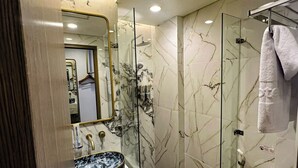 A modern bathroom with a glass-enclosed shower, a marble sink, and a toilet with a towel on it. - d'primahotel PIK Jakarta (Jakarta)