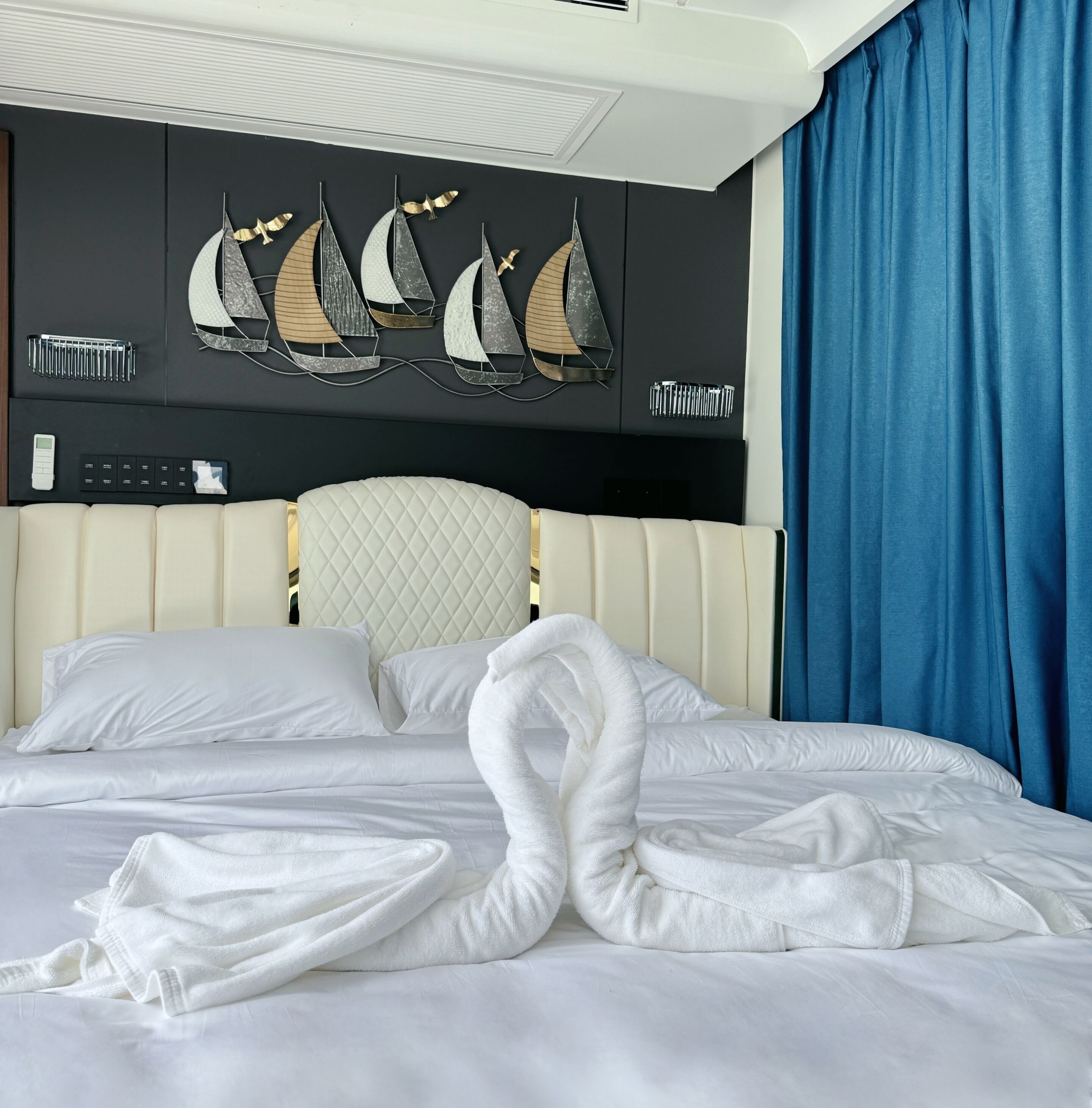 A hotel room with a bed, a headboard with a quilted design, and a wall-mounted air conditioning unit.