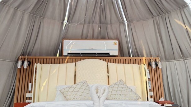 Una camera a tenda con un letto, un condizionatore d'aria a muro e una testiera in legno.
