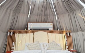 A tent-style room with a bed, a wall-mounted air conditioner, and a wooden headboard. - Thebest Capsule Resort (Kanchanaburi)