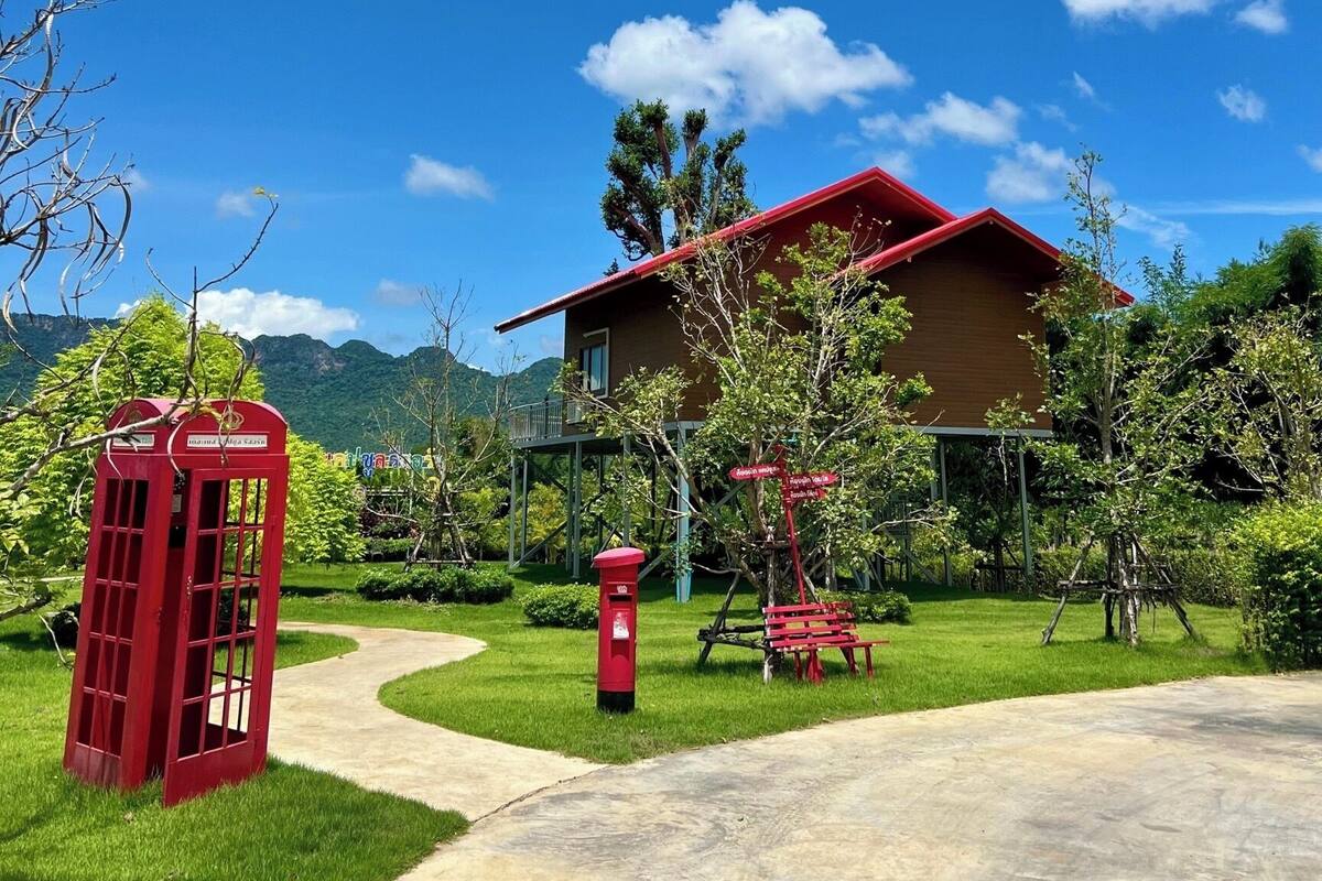 A two-story building with a red roof, surrounded by lush greenery and mountains in the background.