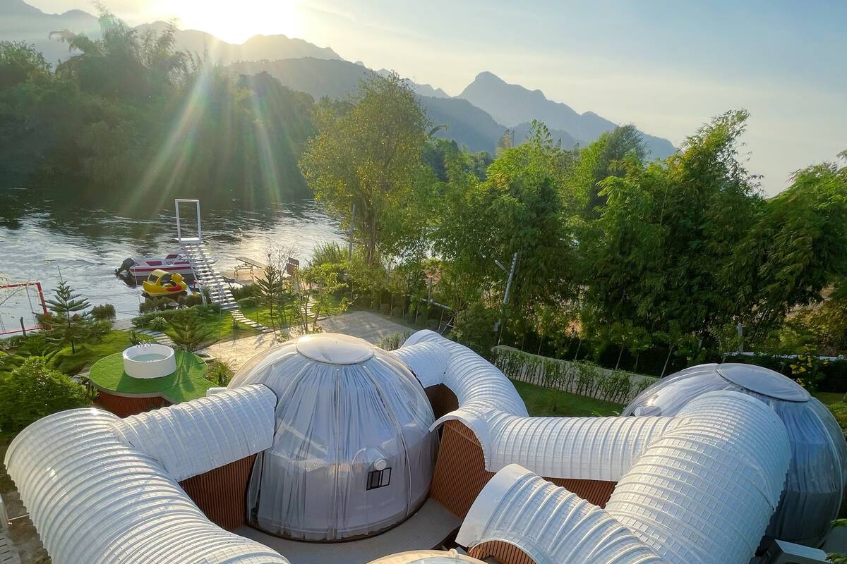 A series of dome-shaped structures with transparent roofs, likely used for accommodation or events, situated by a body of water with mountains in the background.