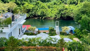 Un resort con un ponte di vetro che si estende su un fiume, circondato da una rigogliosa vegetazione e montagne.