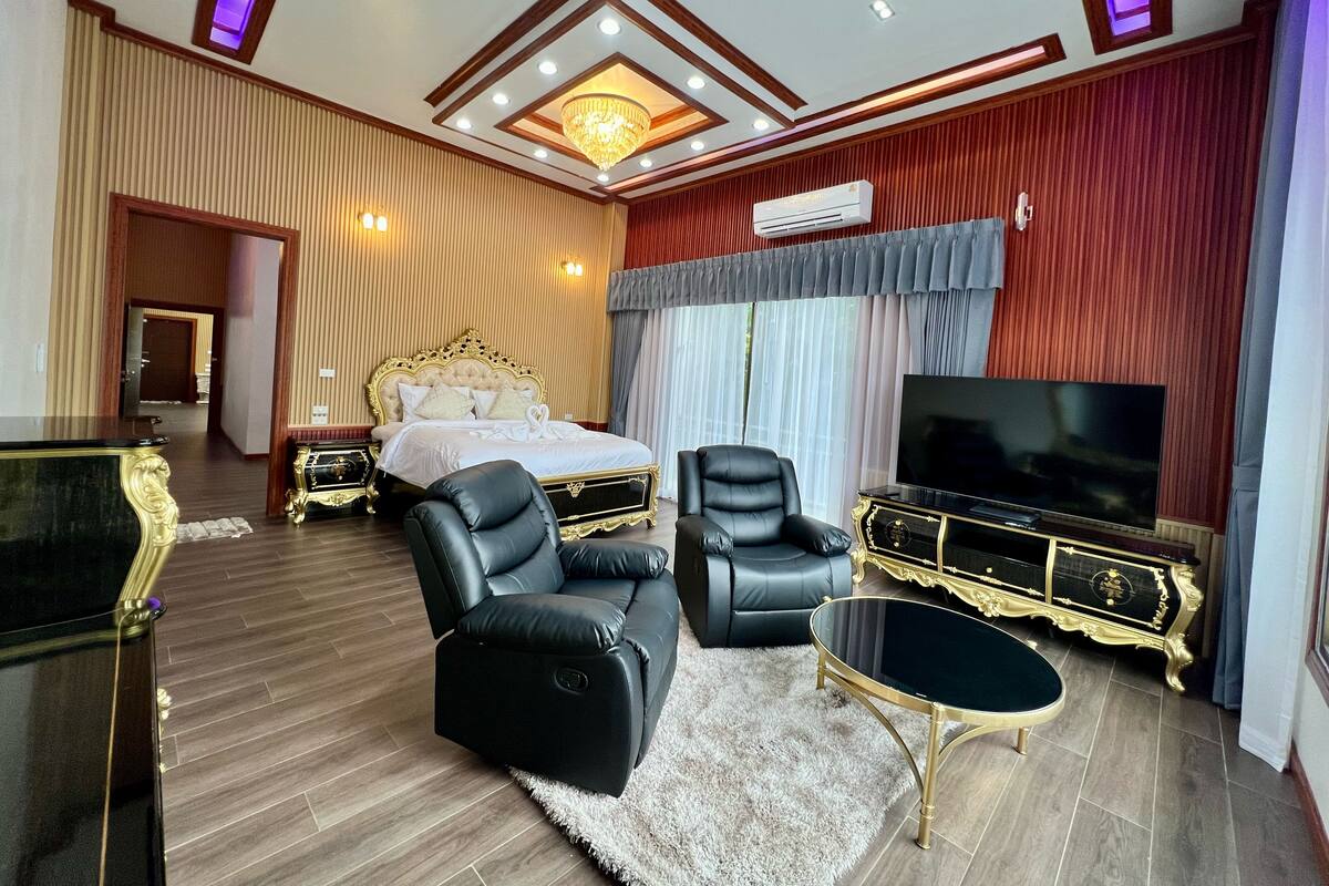 A luxurious bedroom with a large bed, a TV, a sofa, and a gaming table.