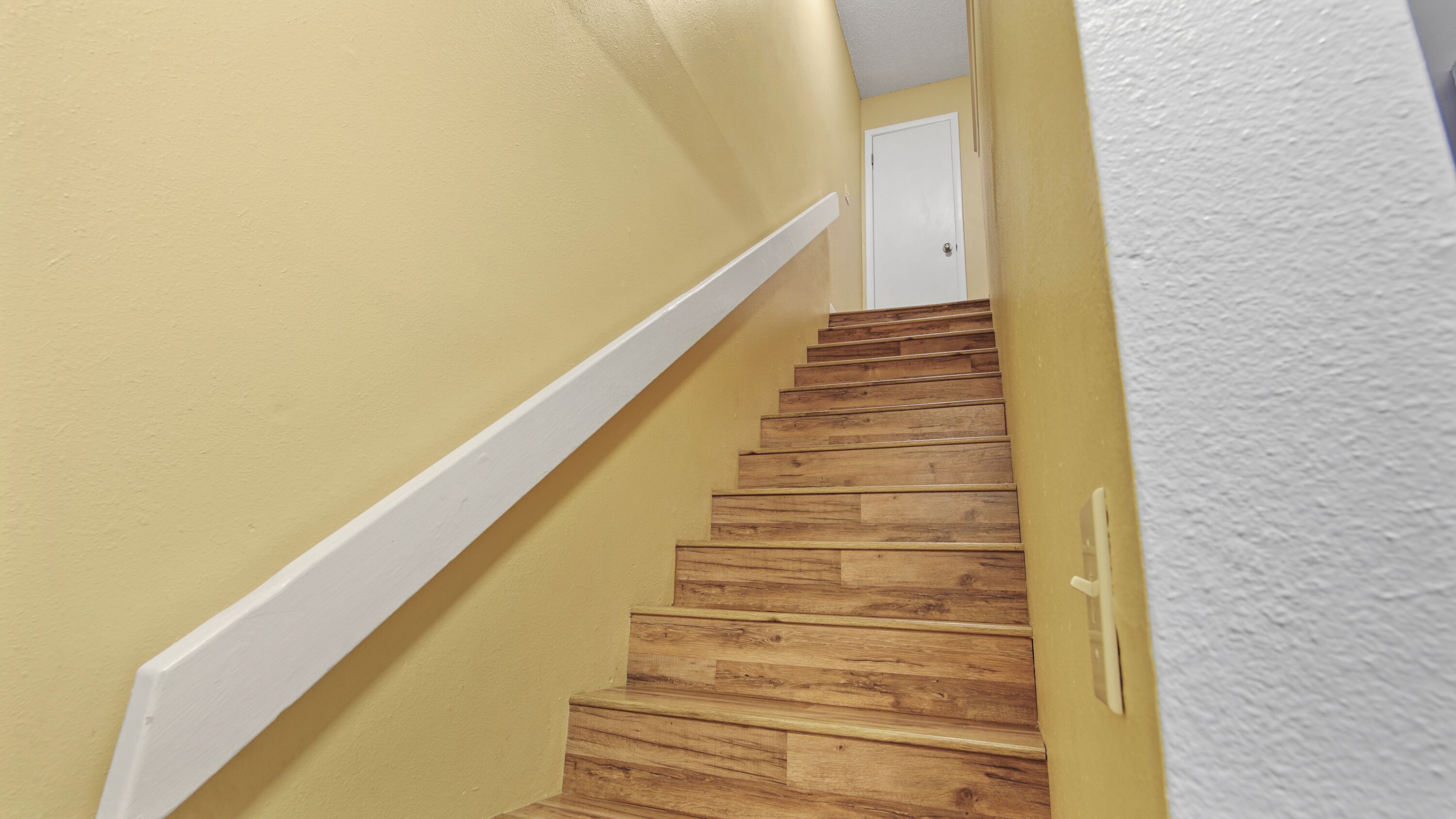 Un escalier en bois, doté d’une rampe blanche, mène à une porte blanche située en haut.