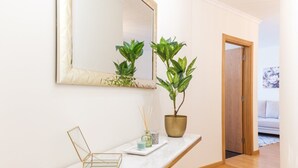 Un pasillo con un banco de mármol, dos plantas en macetas, un espejo y una puerta que da a un salón.