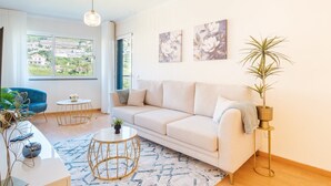 Una sala de estar moderna con un sofá color beige, una mesa redonda y un sillón azul. Hay dos cuadros en la pared y una planta en maceta al lado del sofá.