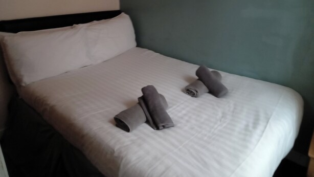 Un lit bien fait, avec des draps blancs et deux serviettes enroulées posées sur le lit.