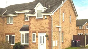 A two-story brick house with a white door, windows with shutters, and a small front garden.