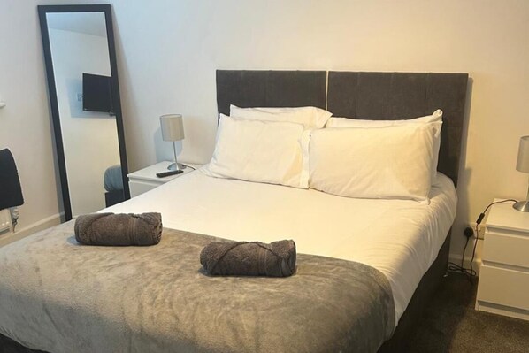A neatly made bed with white linens and two rolled towels on the bed.