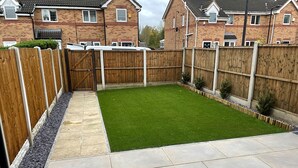 A backyard with a paved patio, a wooden fence, and a well-maintained lawn.