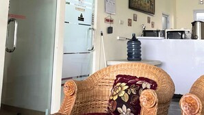 A reception area with a wicker chair, a water dispenser, and a painting on the wall. - Djuragan Kamar Macan Kumbang (Palembang)