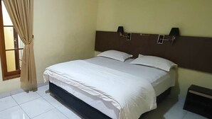 A hotel room with a bed, curtains, a nightstand, and a wall-mounted lamp. - Djuragan Kamar Macan Kumbang (Palembang)