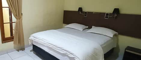 Una habitación de hotel con cama, cortinas, mesita de noche y lámpara de pared.