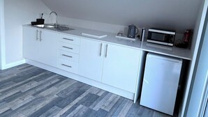 Een moderne keuken met witte kastjes, een roestvrijstalen spoelbak, een magnetron en een kleine koelkast.