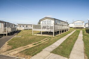 A row of mobile homes with a grassy area and a paved walkway.