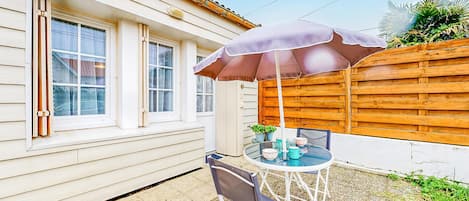 A patio with a table and chairs, a wooden fence, and a house with white siding and windows.