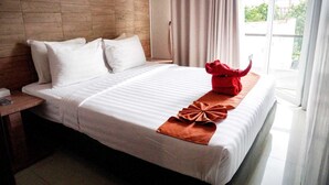 A hotel room with a large bed, a wooden headboard, a nightstand, and a view of the outdoors through a window. - Andelir Hotel Simpang Lima Semarang  (Semarang)
