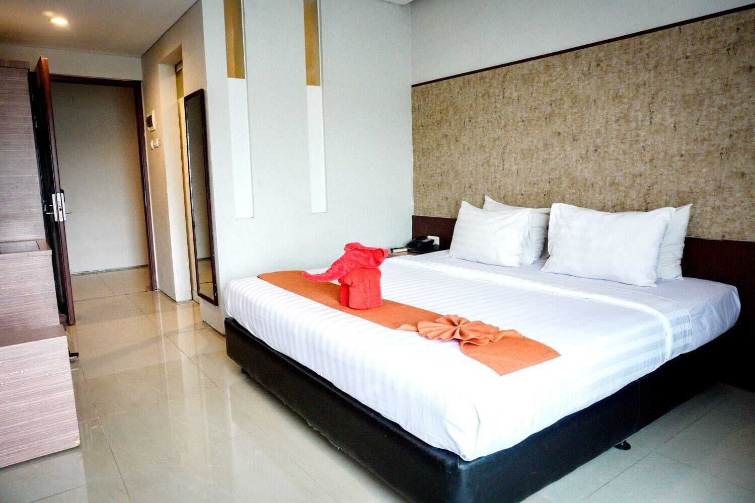 A hotel room with a large bed, white bedding, and a red towel on the bed.