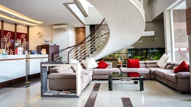 A modern hotel lobby with a curved staircase, a reception desk, a seating area with sofas, and a large aquarium. - Andelir Hotel Simpang Lima Semarang  (Semarang)