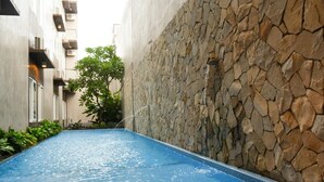 A swimming pool with a stone wall on one side and a building on the other. - Andelir Hotel Simpang Lima Semarang  (Semarang)