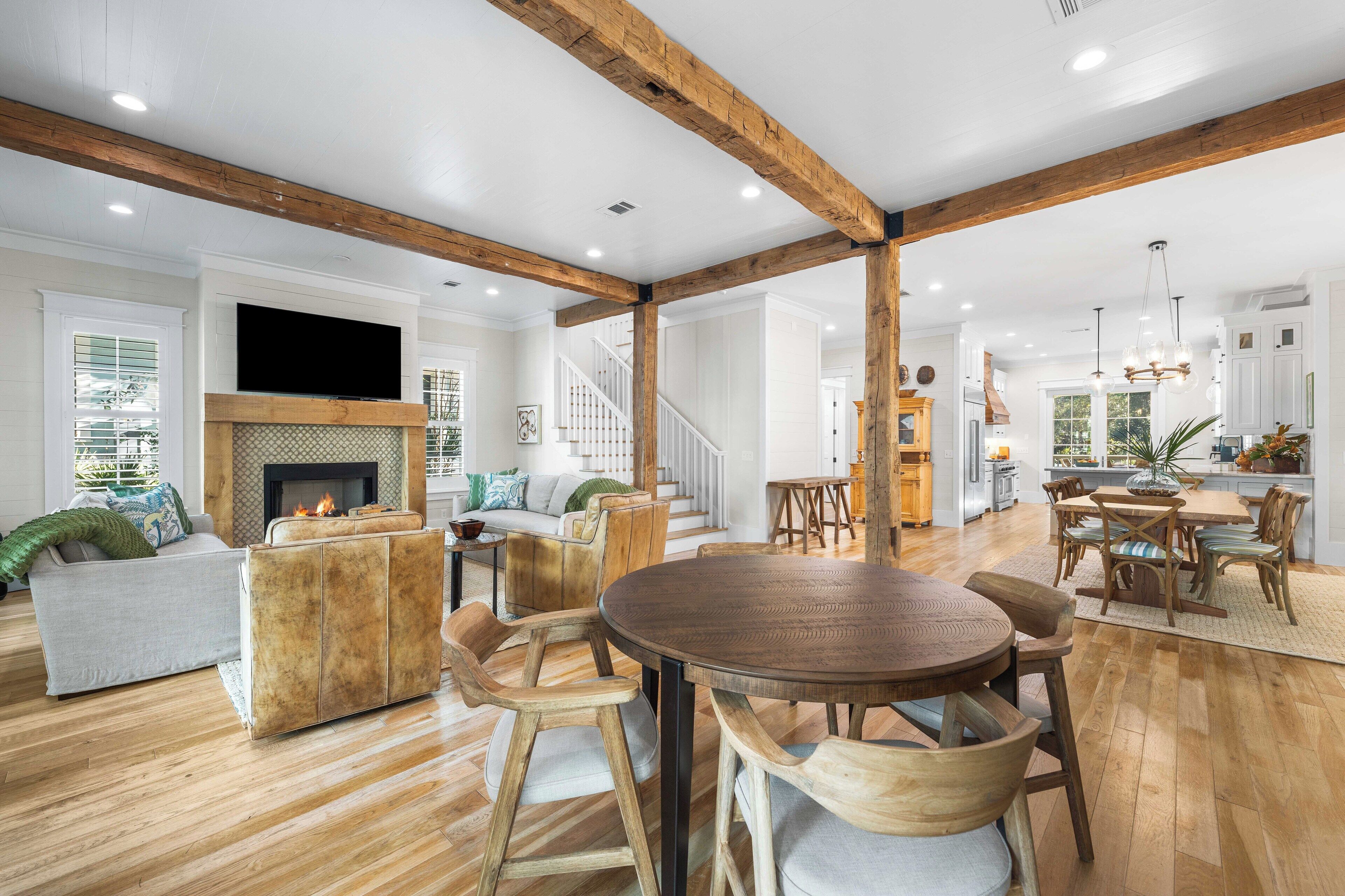 Amplia sala de estar con chimenea, vigas de madera, mesa de comedor y escalera que conduce a otro nivel.