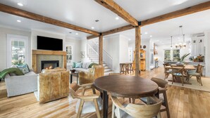 A spacious living area with a fireplace, wooden beams, a dining table, and a staircase leading to another level. - WaterColor Beach Retreat Offering a Private Pool, Golf Cart, And Full Access to the Beach Club! (Santa Rosa Beach)