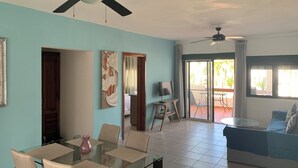 Amplia sala de estar con mesa de comedor de vidrio, asientos cómodos, ventiladores de techo y un balcón con vistas.