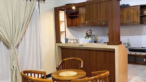A compact kitchen with wooden cabinets, a dining table with chairs, and a kitchen island. - DAlvin Homestay: Cozy, Central Labuan Bajo, Near Airport–Perfect for Your Stay! (Kabupaten Labuan Bajo)