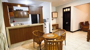 A spacious kitchen with wooden cabinets, a dining area with a round table and four chairs, and a black door. - DAlvin Homestay: Cozy, Central Labuan Bajo, Near Airport–Perfect for Your Stay! (Kabupaten Labuan Bajo)