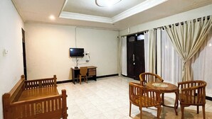 A spacious living room with a sofa, a coffee table, and two chairs. There is a television on a stand, a small desk, and a door in the background. - DAlvin Homestay: Cozy, Central Labuan Bajo, Near Airport–Perfect for Your Stay! (Kabupaten Labuan Bajo)