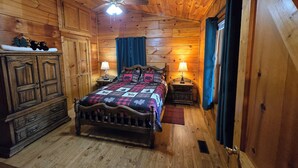 A wooden cabin bedroom with a bed, two bedside tables with lamps, a wardrobe, and a ceiling fan.