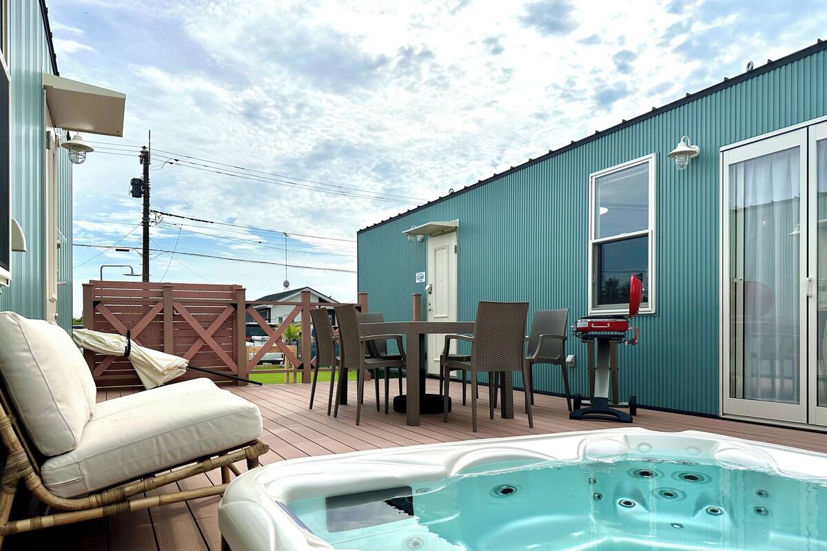 A hot tub on a wooden deck with outdoor furniture, a table, and chairs.