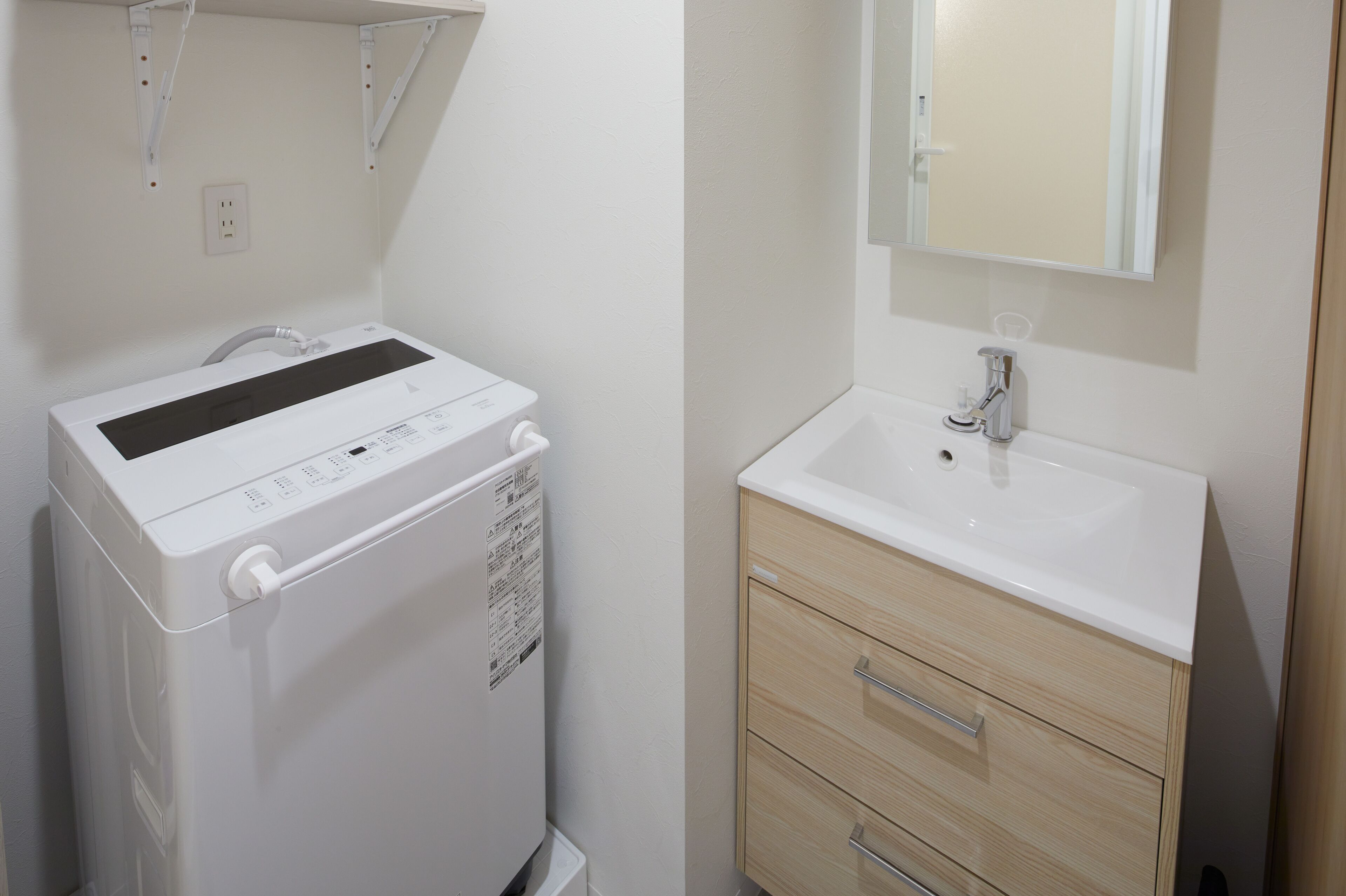 A compact, modern bathroom with a white washing machine, a sink, and a mirror.