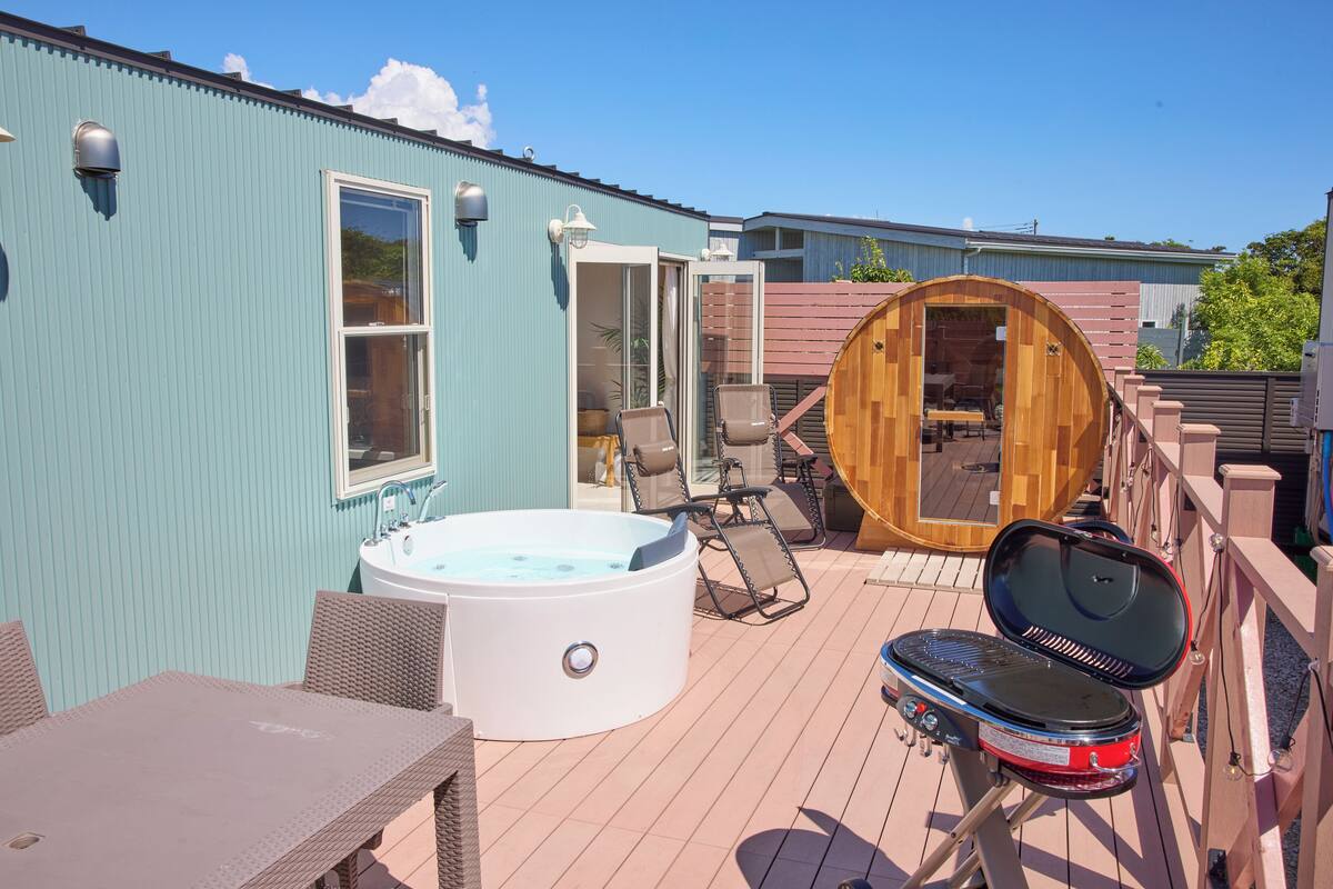 A deck with a hot tub, outdoor seating, and a grill.