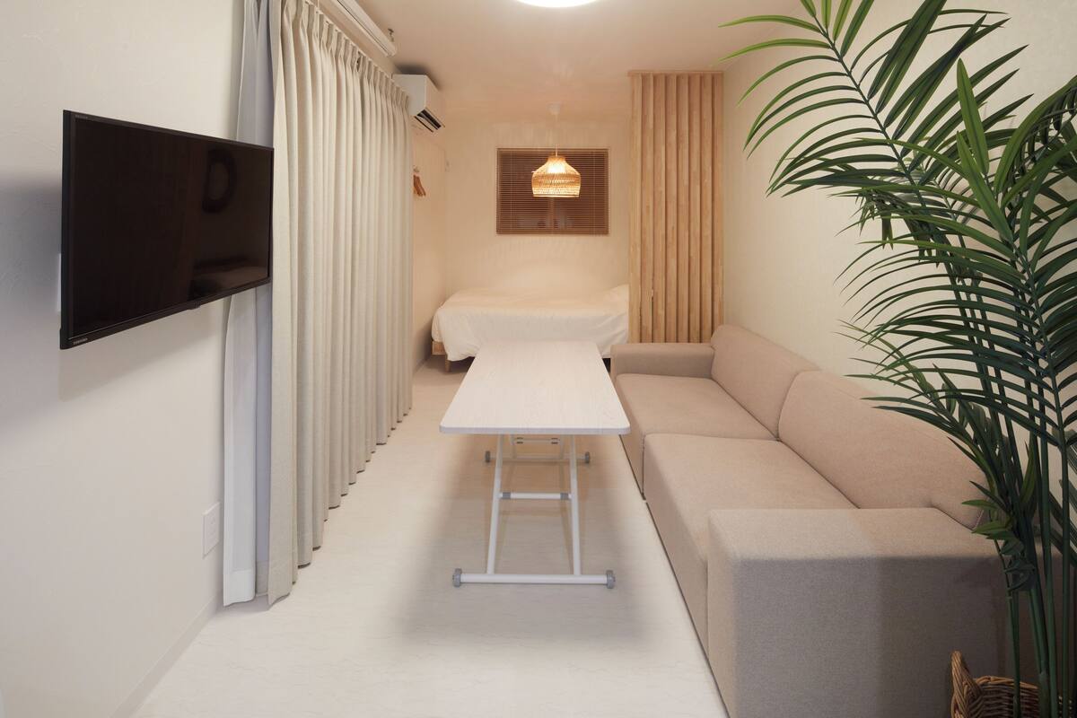 A compact living space with a flat-screen TV mounted on the wall, a foldable table, a sofa, and a potted plant.