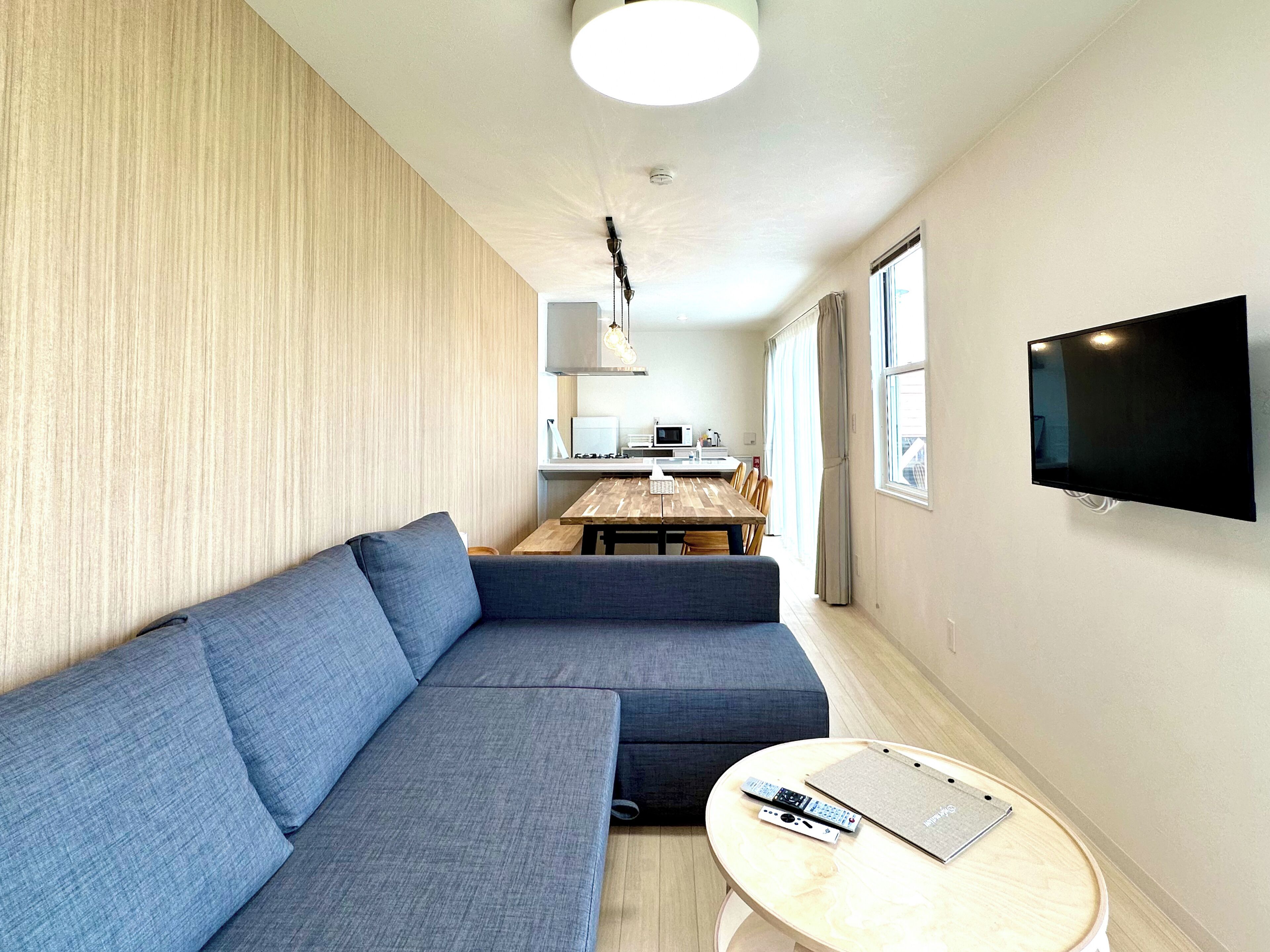 Una sala de estar moderna con un sofá seccional, una mesa de comedor y un televisor de pantalla plana montado en la pared.