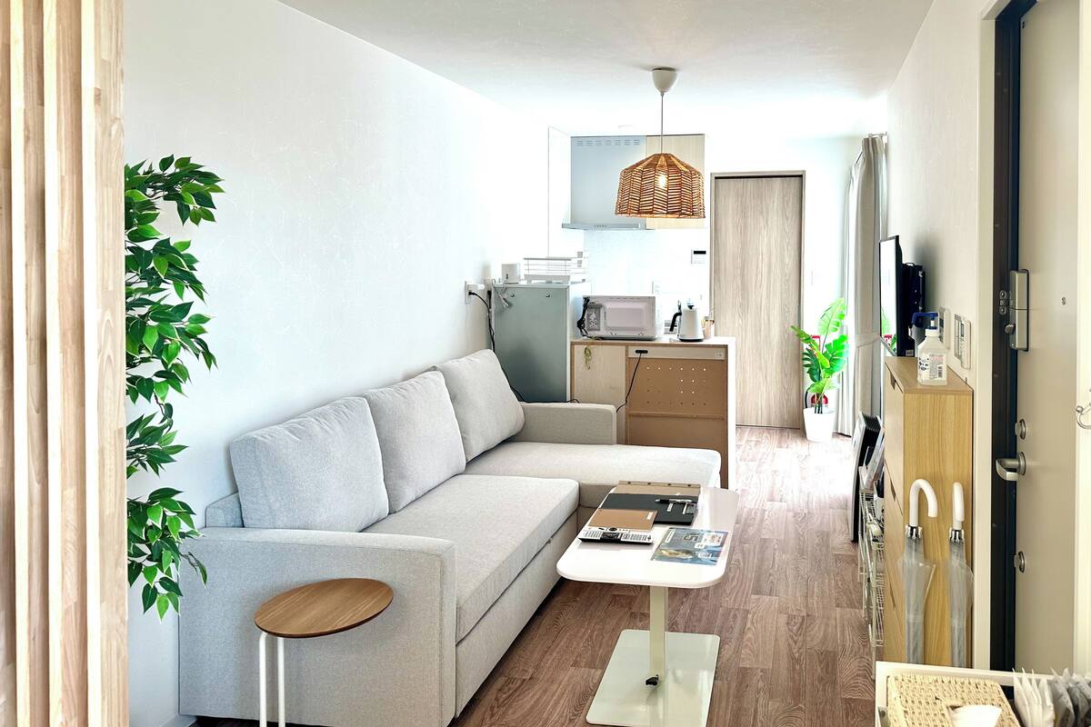 A modern living room with a sofa, a small round table, a kitchen area with a microwave, and a hanging light fixture.