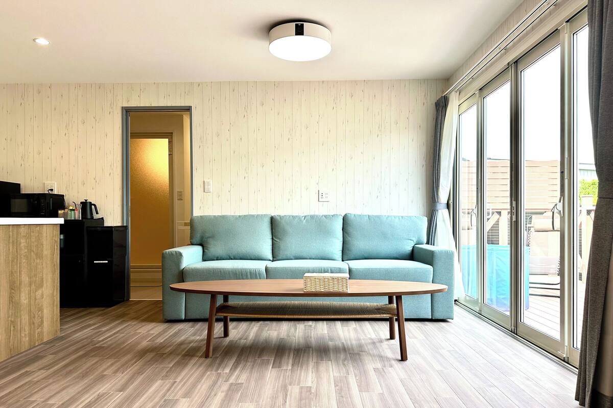 A modern living room with a light blue sofa, a wooden coffee table, and a large window with curtains.