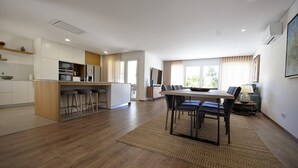 Una cocina moderna con una isla central, un comedor con mesa y sillas, y una sala de estar con sofá y televisor.